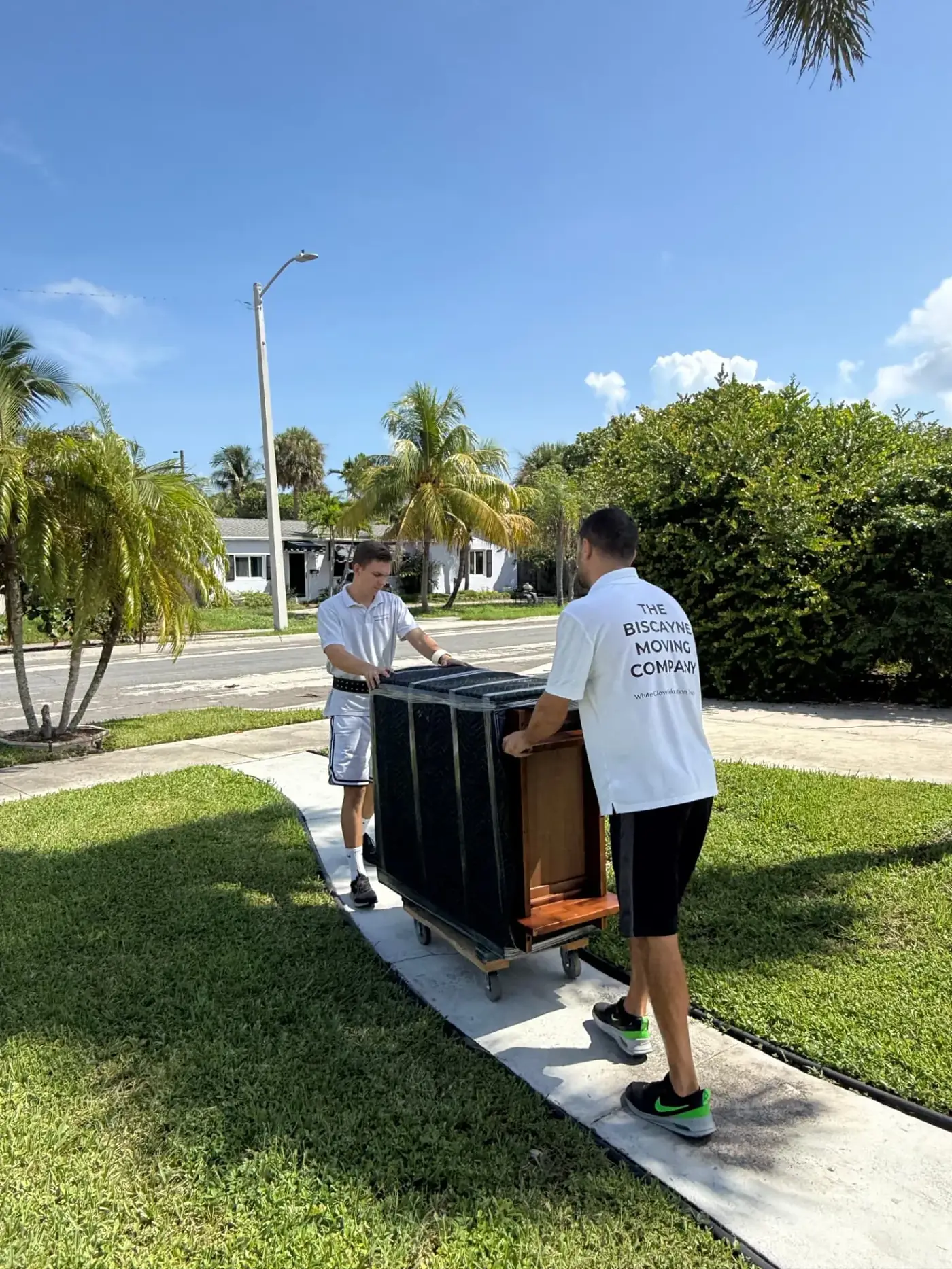 Biscayne Moving Co. packers carrying a wrapped dresser on a dolly in Miami